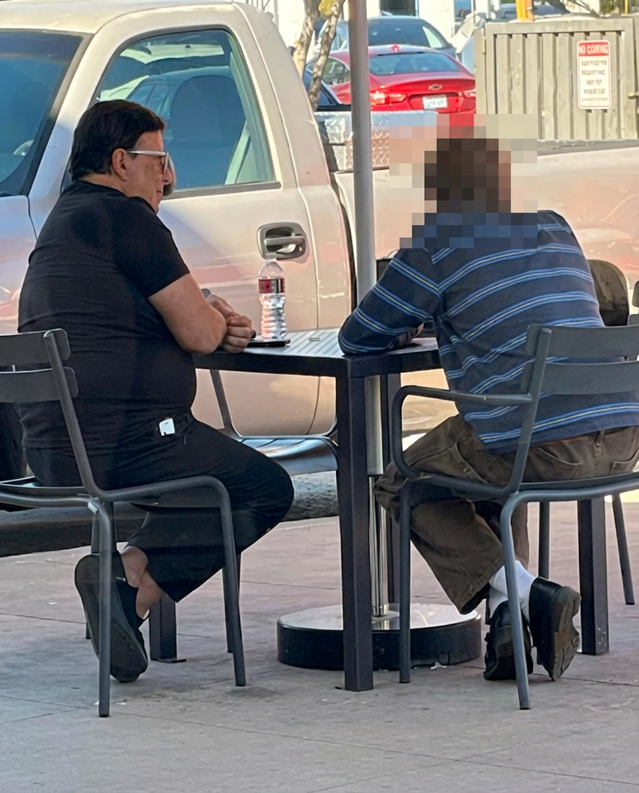 Emil Barham seated at an outdoor table across from a student, whose face has been blurred